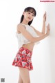 A woman in a white top and red skirt leaning against a wall.