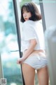 A woman in a white shirt and white panties leaning against a window.