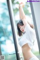 A woman in a white shirt is posing by a window.