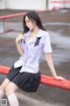 A woman in a school uniform sitting on a red railing.