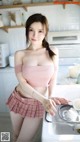 a woman in a pink top and plaid skirt standing in a kitchen