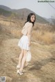 A woman in a white skirt and heels standing on a dirt road.