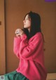 A woman in a pink sweater sitting on a bed holding a cup of coffee.