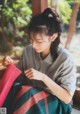 A woman sitting on a window sill knitting a piece of fabric.