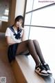 A woman in a school uniform sitting on a window sill.