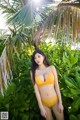 A woman in a yellow bikini standing in front of a palm tree.