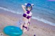 A woman in a purple bikini sitting on a beach next to the ocean.