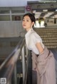 A woman in a white shirt and a pink coat leaning against a railing.