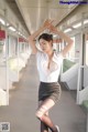 A woman in a white shirt and black skirt on a train.