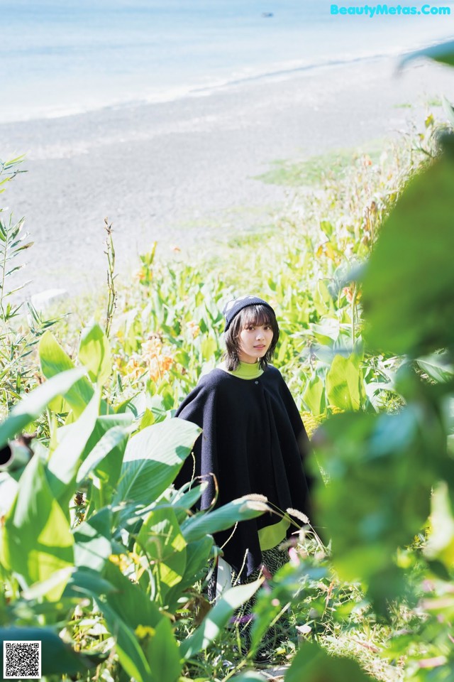 A woman standing in a field of tall grass next to the ocean.