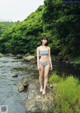 A woman in a bikini standing on a rock by a river.