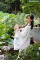 A woman in a white dress holding a fan in a garden.