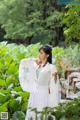 A woman in a white dress holding a fan in a garden.