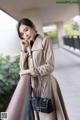 A woman in a beige trench coat leaning against a railing.