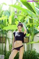 A woman in a black bikini posing in front of a banana tree.