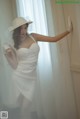 A woman in a white dress and hat leaning against a wall.