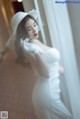 A woman in a wedding dress and hat leaning against a window.