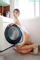 A woman in a maid outfit is sitting on the floor next to a washing machine.