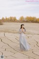 A woman in a long dress standing in the middle of a desert.