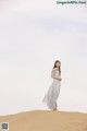 A woman in a white dress standing on top of a sand dune.