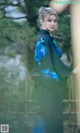 A woman in a green and blue dress standing in front of a bamboo fence.