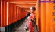 A woman in a kimono standing in front of a row of orange torii gates.