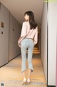 A woman in a pink blouse and jeans walking down a hallway.