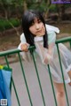 A woman in a white dress leaning against a green fence.