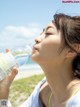 A woman drinking water from a bottle on the beach.